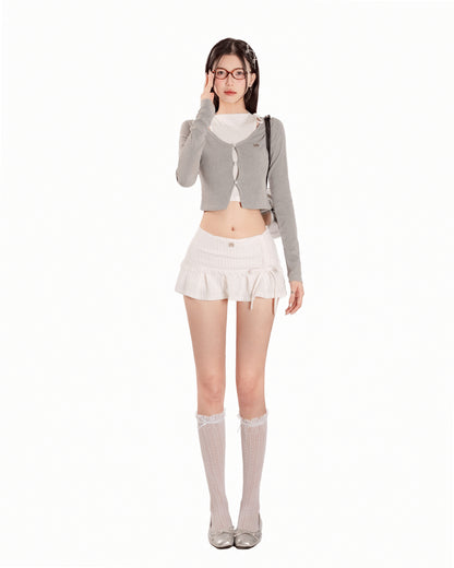Woman wearing a gray cardigan, white top, and skirt with knee-high socks on a white background