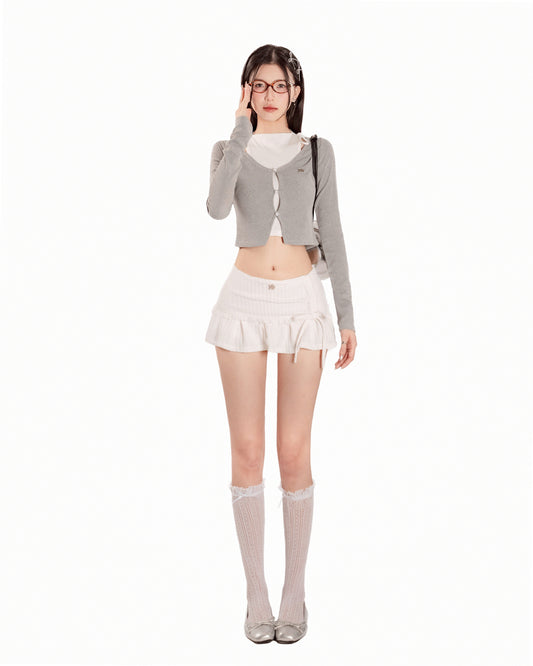 Woman wearing a gray cardigan, white top, and skirt with knee-high socks on a white background