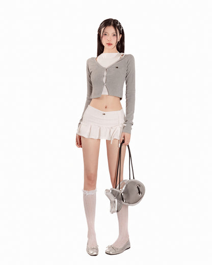 Woman wearing a gray cardigan, white skirt, and white socks with a small bag on a white background