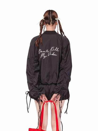Person wearing a black jacket with text, holding red high-heeled shoes on a white background