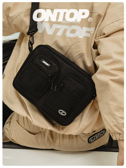 Black crossbody bag with 'ONTOP' branding worn by a person in a beige jacket.