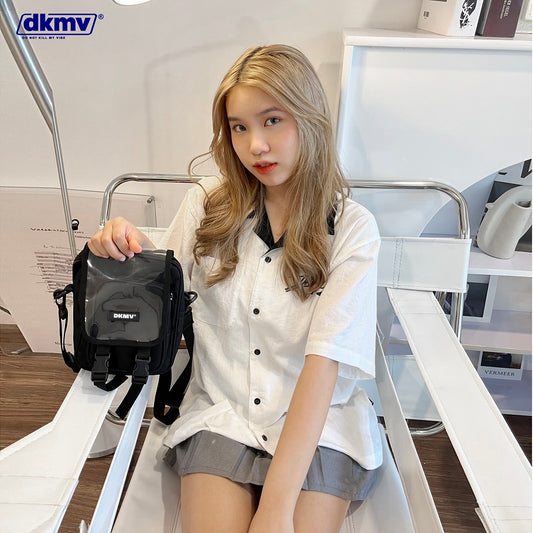 Woman holding a black bag with 'dkmv' branding in an indoor setting