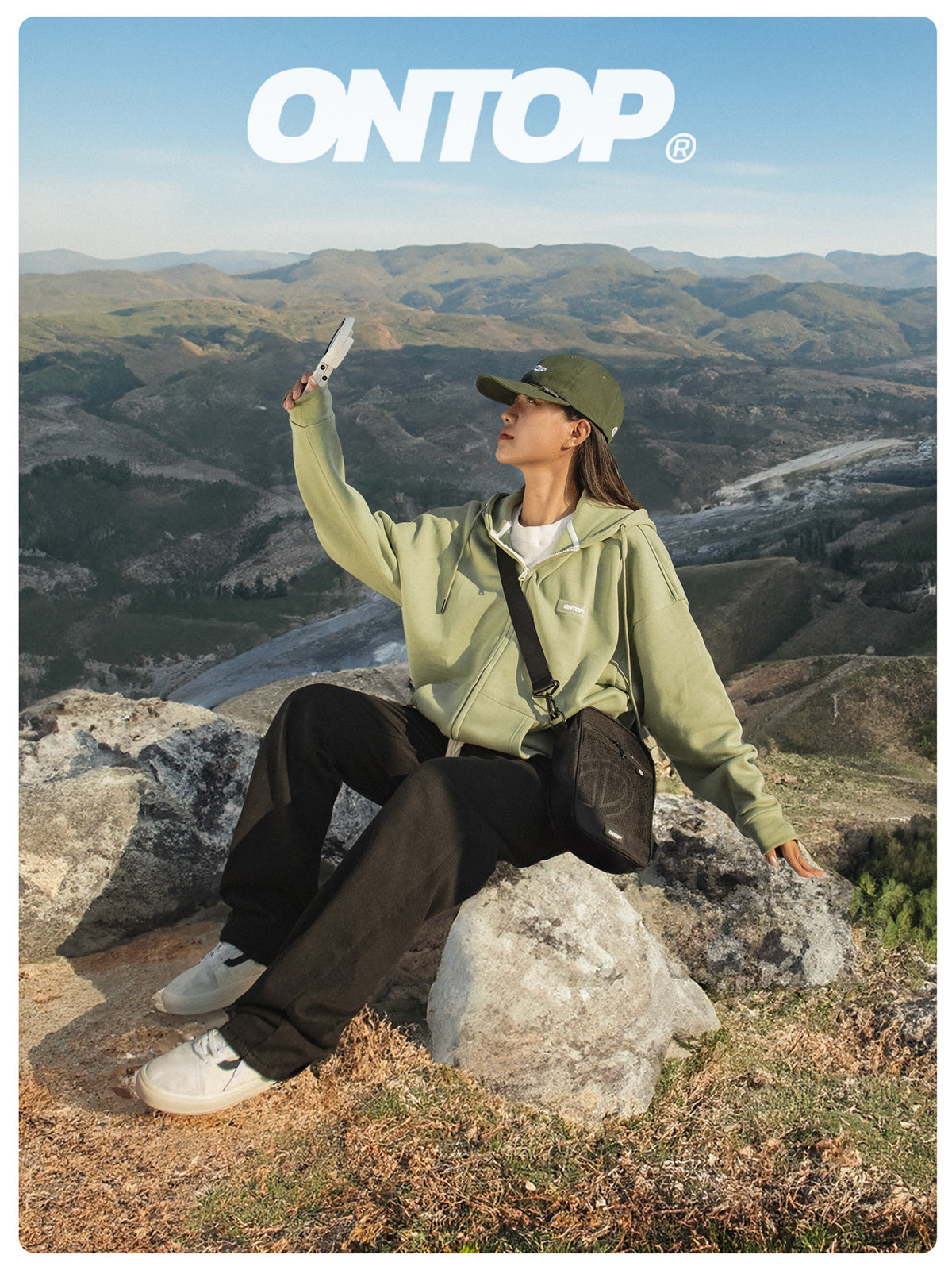 Person sitting on a rock taking a selfie with scenic mountains in the background, featuring the brand 'ONTOP'.