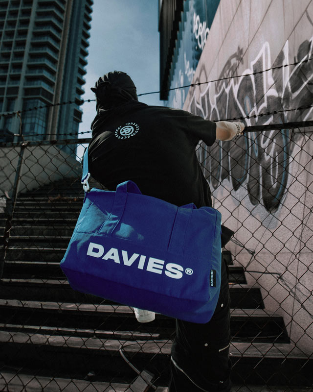 Person holding a blue 'DAVIES' bag against a graffiti-covered wall.