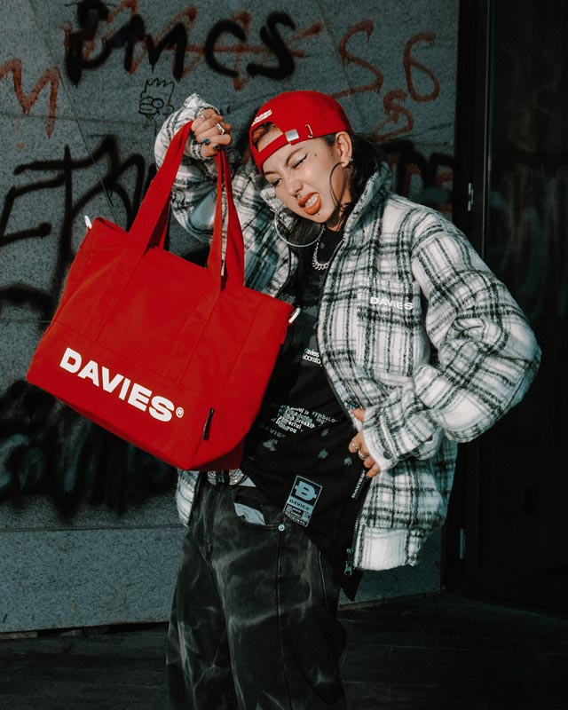 Person holding a red 'DAVIES' bag against a graffiti-covered wall.