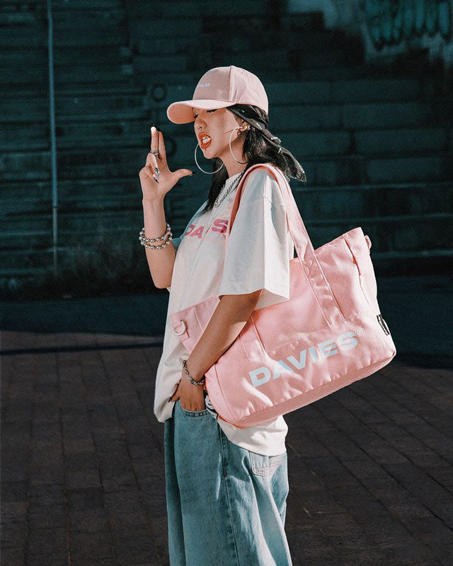 Person wearing a pink cap and holding a pink 'DAVIES' bag against a dark background