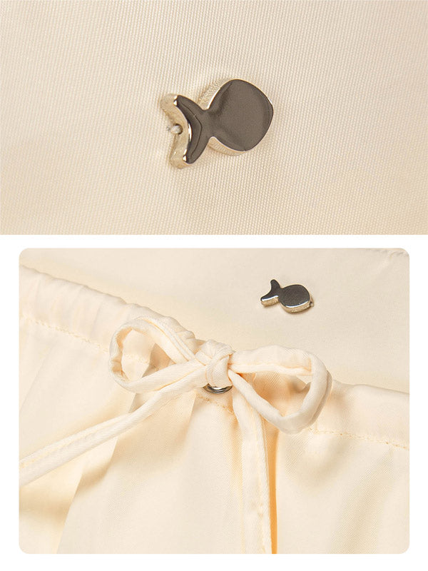 Close-up of a beige drawstring bag with a fish-shaped tag on a beige background.