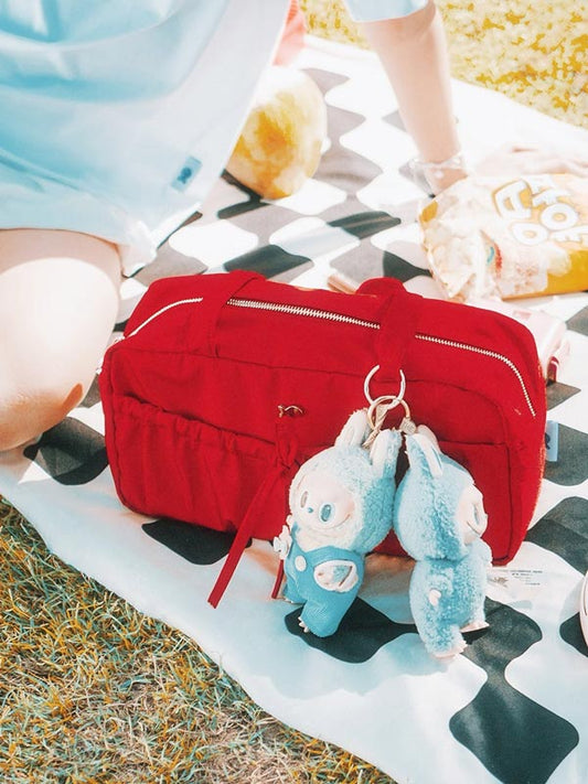 Red bag with plush keychains on a checkered blanket outdoors