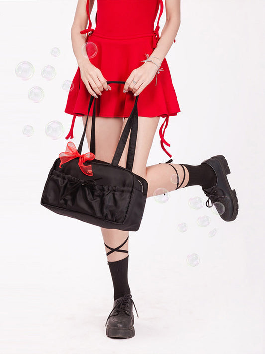 Person wearing a red dress and black shoes holding a black handbag with a red bow on a white background.