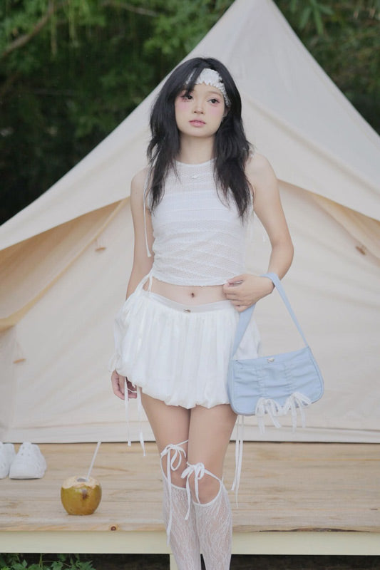 Woman in a white outfit with a blue bag standing in front of a tent.