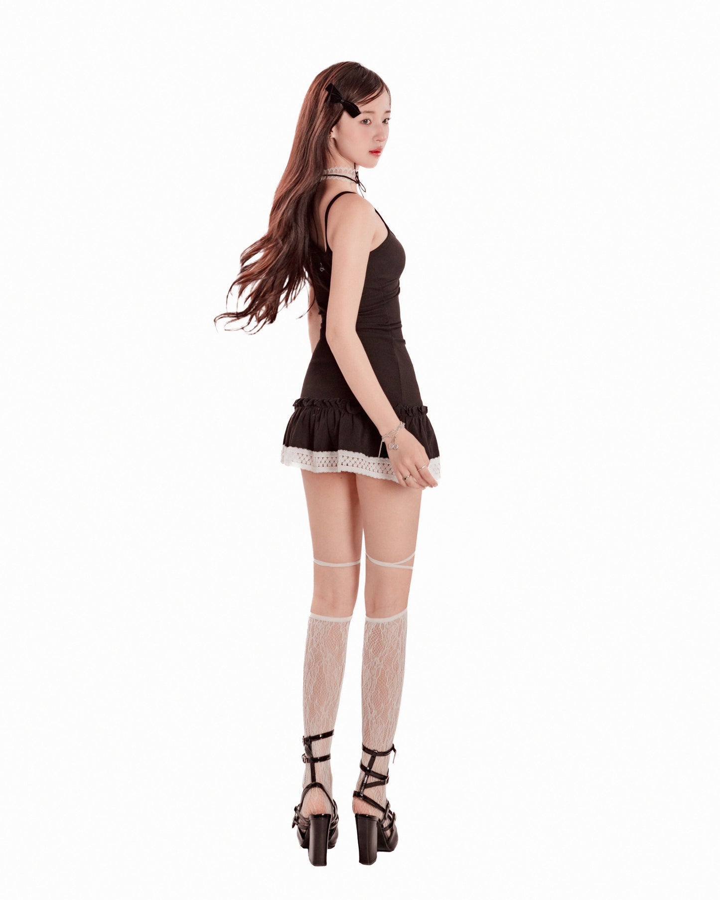 Woman wearing a black dress with lace trim and fishnet stockings on a white background