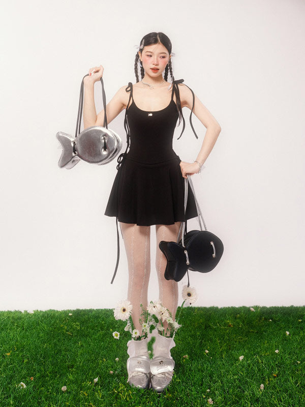 Woman in a black dress holding a fish-shaped bag on a grassy surface with a white background