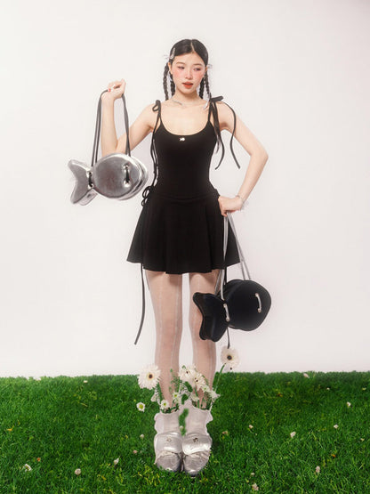 Woman in a black dress holding a fish-shaped bag on a grassy surface with a white background