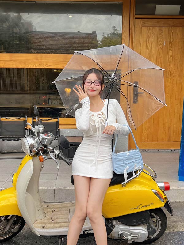 Woman holding a transparent umbrella in front of a yellow scooter and wooden door.