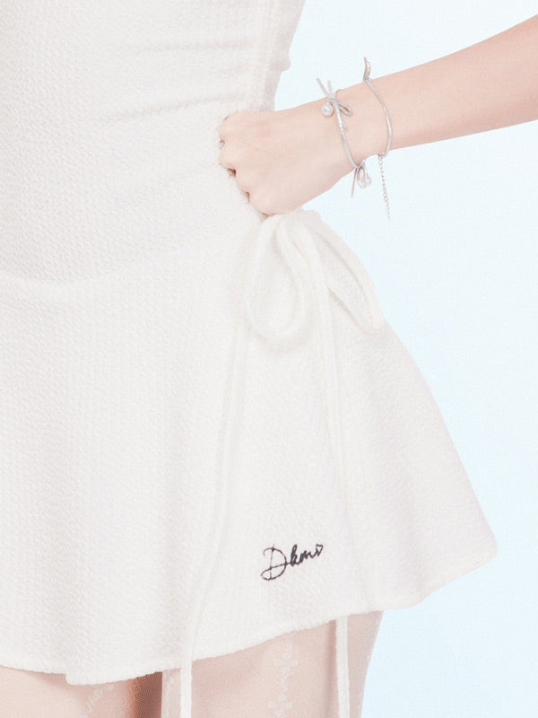 White skirt with 'Delave' embroidery held by a hand on a light pink background