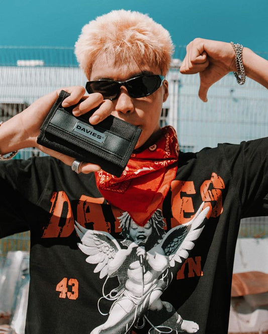 Person wearing a black t-shirt with graphic designs, holding a black wallet with 'DAVIES' branding.